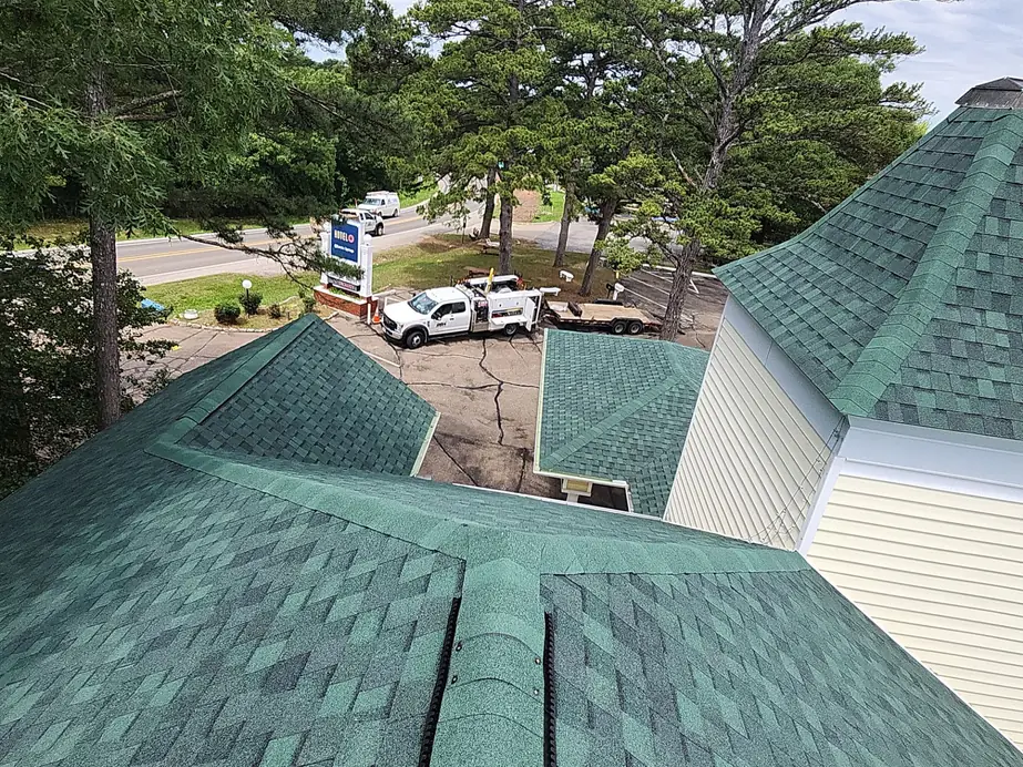 Drone view over new green shingle roof hips with the JAD work truck and trailer in the lot