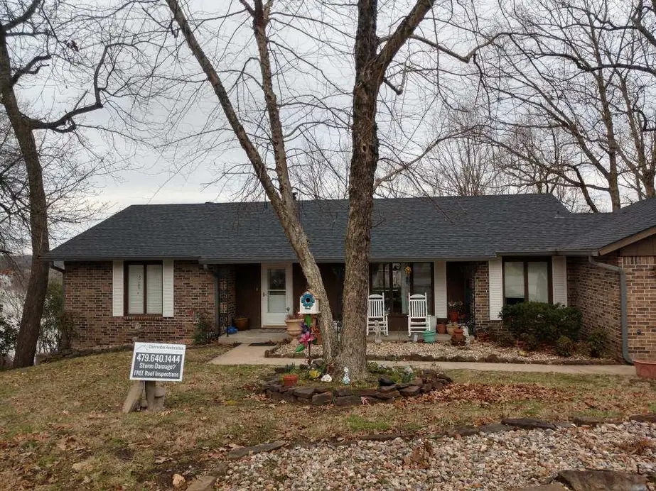 Brick ranch home with a new charcoal roof and a free roof inspection yard sign on the lawn